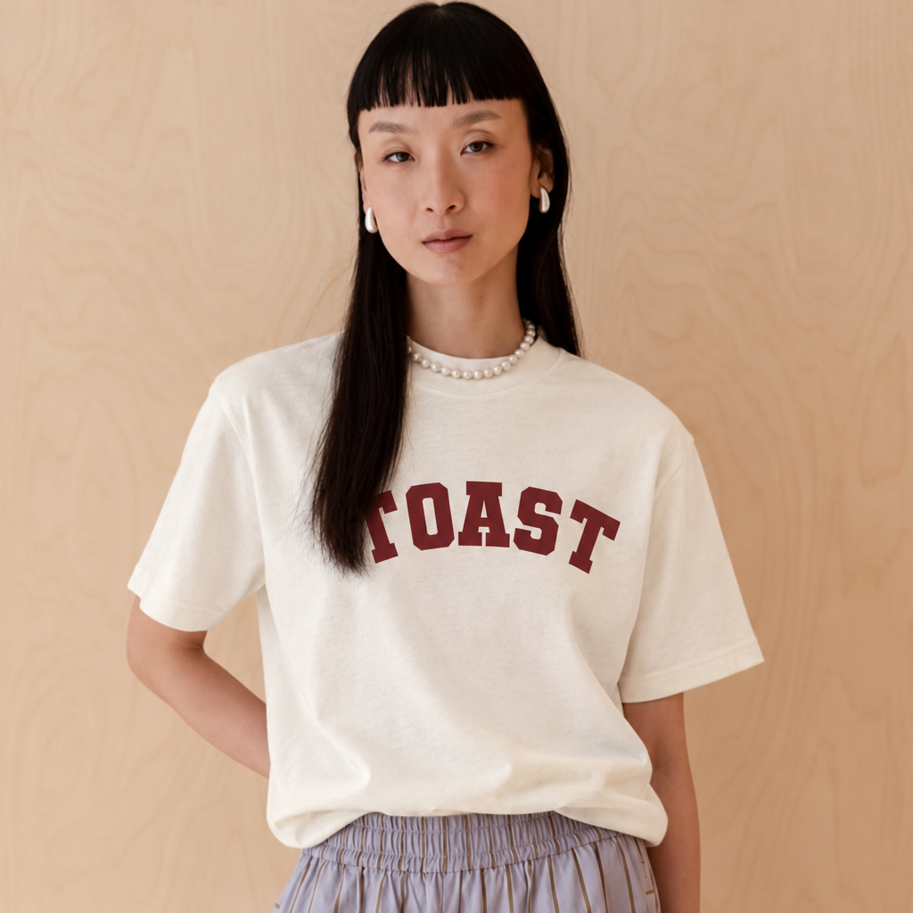 cream coloured tshirt on an asian woman it says toast in a varsity print in burgundy 