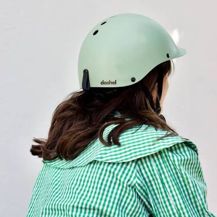 A person shown from the back wearing a matte mint green helmet with the brand name 'dashel' printed in black on the side, paired with a green and white striped shirt against a plain light gray background.