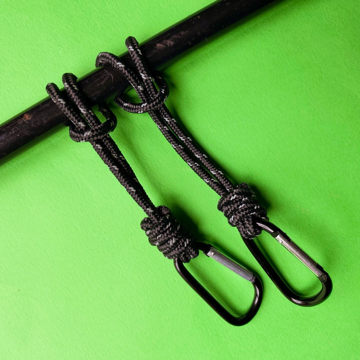 Two black rope lanyards with knotted loops and black metal carabiners, displayed on a bright green background. high-vis-paracord-bag-straps-with-carabiner-clips