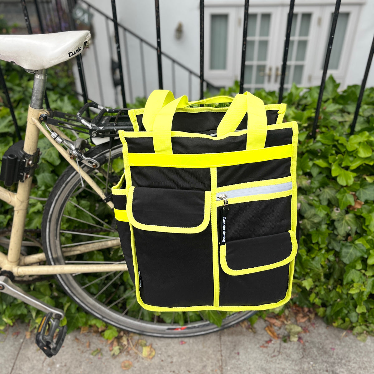 Neon market shopper pannier - Goodordering shown on bike pannier rack against a metal fence