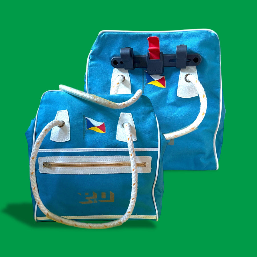 Blue bag with white handles and a colorful flag on a green background upcycled to a bike pannier bag 
